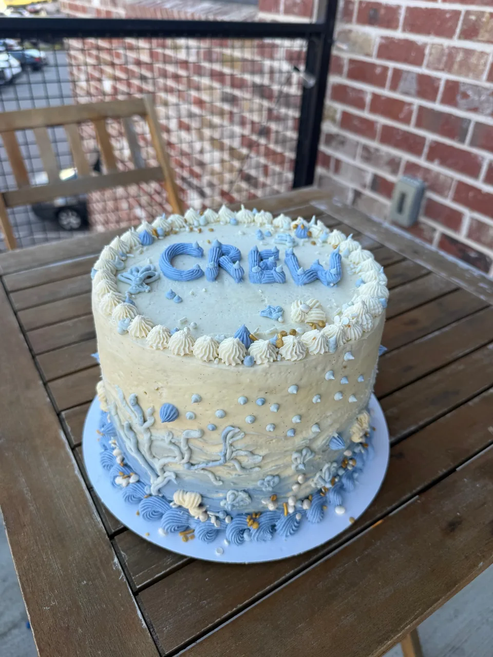 Cream and blue buttercream cake with a name on top and piped coral and shells on the side