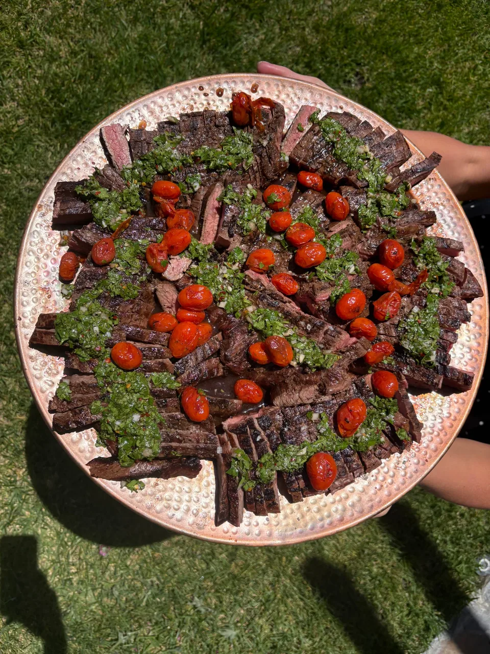 Platter of sliced flank steak with chimichurri and blistered tomatoes