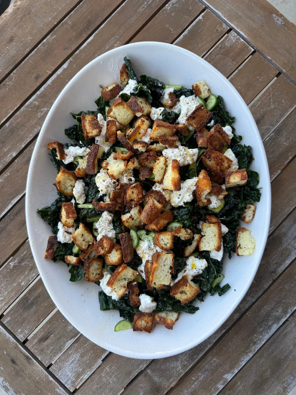 Lacinato kale salad with torn burrata, cucumber and toasted croutons in a white oval bowl