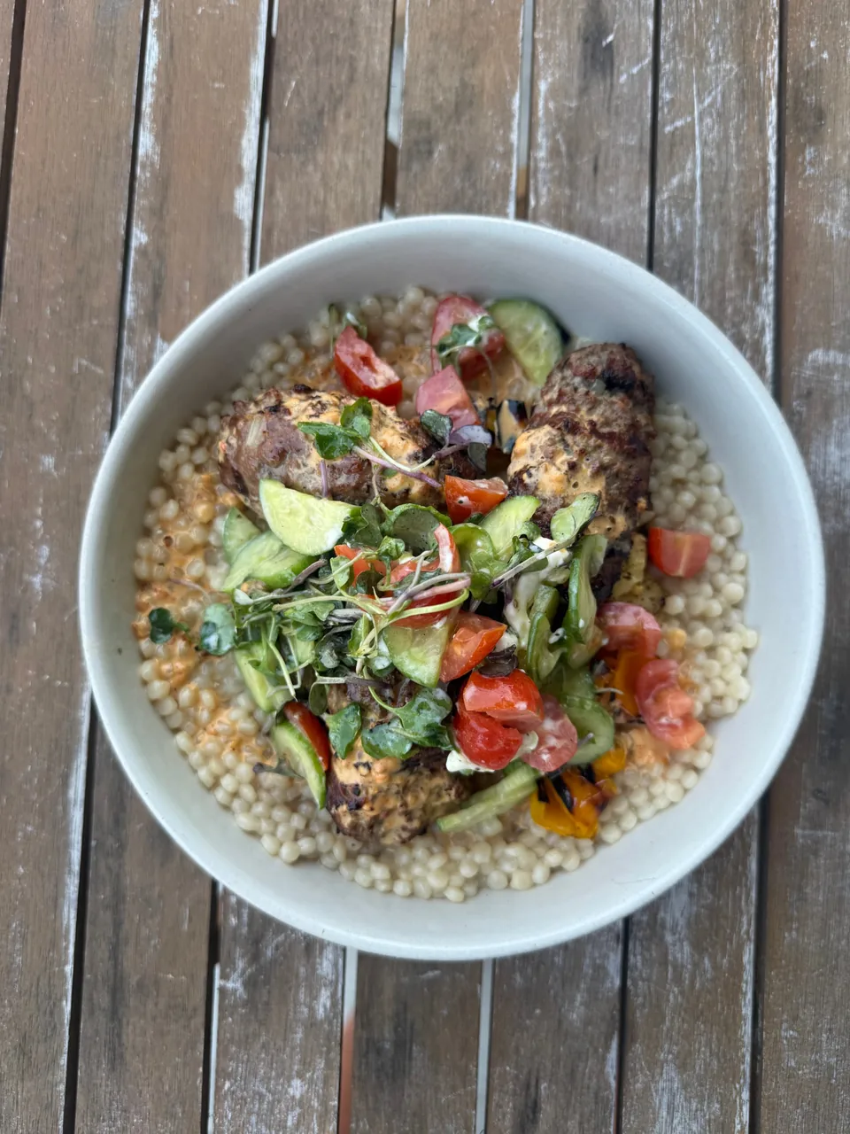 Grilled kofta over pearl couscous with tomato, cucumber and microgreens