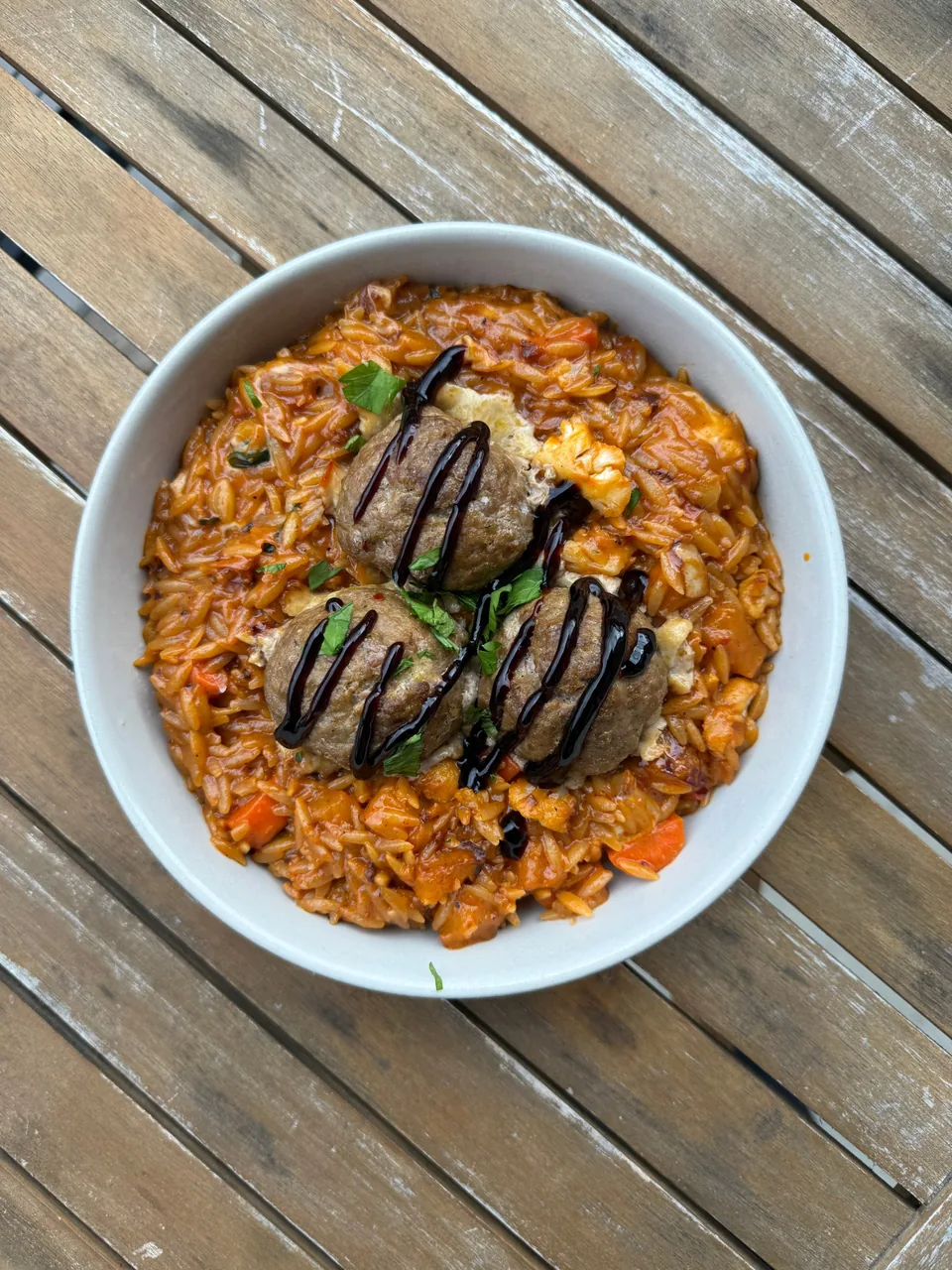 Bowl of tomato orzo with vegetables, topped with meatballs, balsamic and parsley