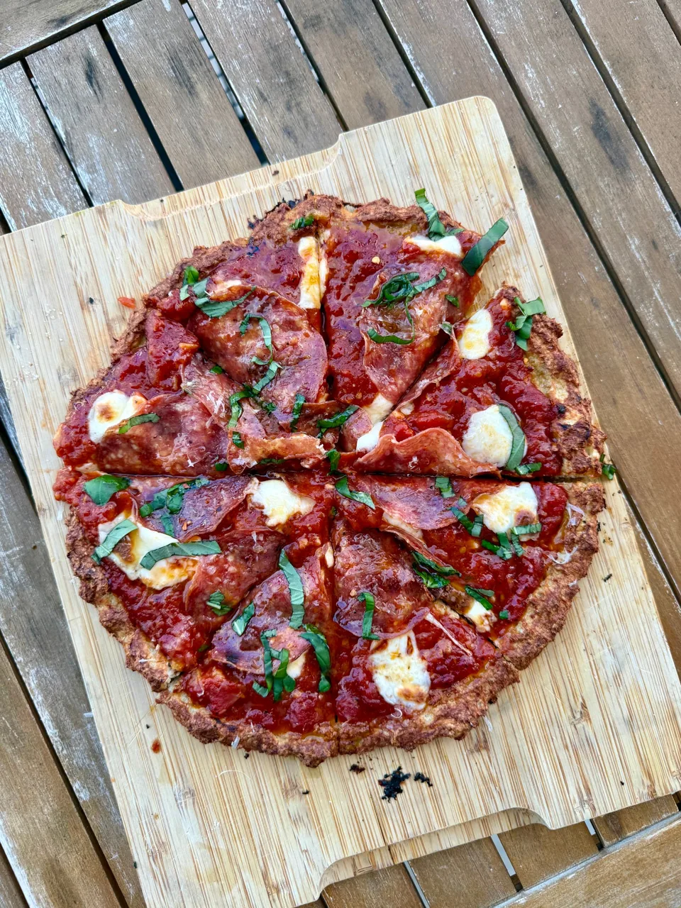 Pizza with tomato sauce, salami, mozzarella and ribbons of basil on a wood board
